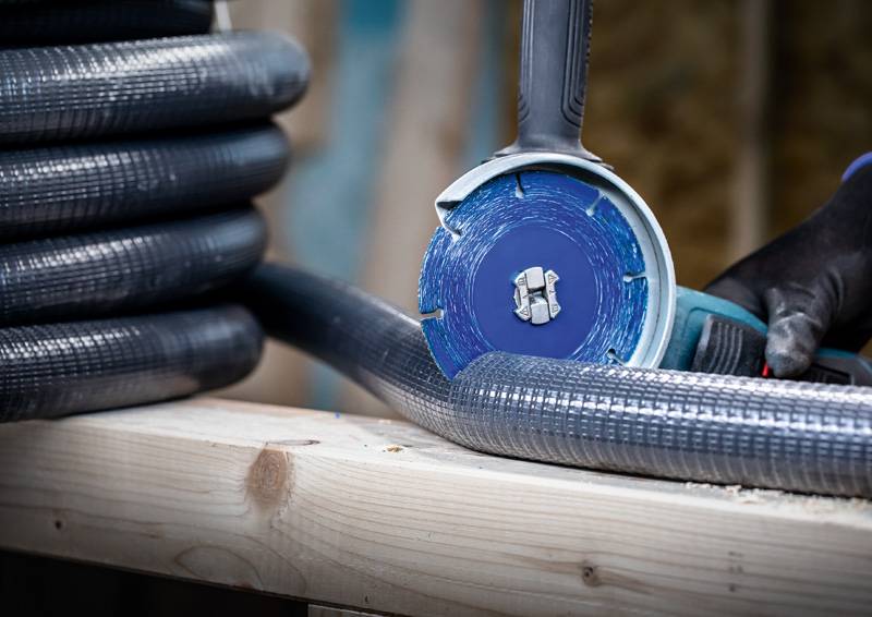 Person benutzt eine blaue Kreissäge, um eine weiße Wand zu schneiden, trägt schwarze Handschuhe für die Sicherheit.