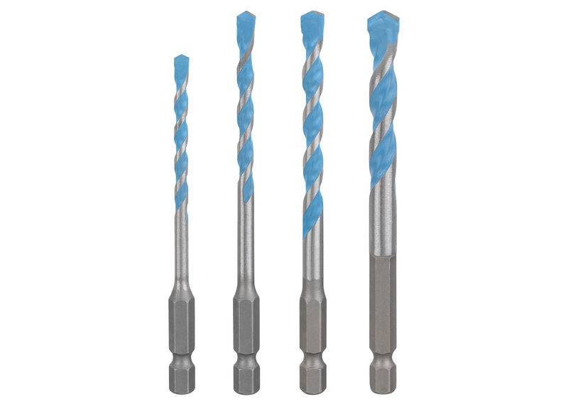 Eine behandschuhte Hand hält einen Elektroschrauber gegen eine gekachelte Wand und deutet eine Aktion des Montierens oder Reparierens in einer modernen Inneneinrichtung an.