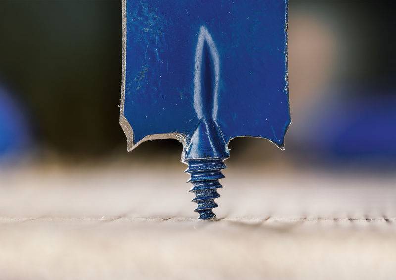 Ein blauer Holzbohrer mit spitzer Spitze und scharfen Kanten steht aufrecht auf einer hellen Holzoberfläche und ist zum Bohren bereit.