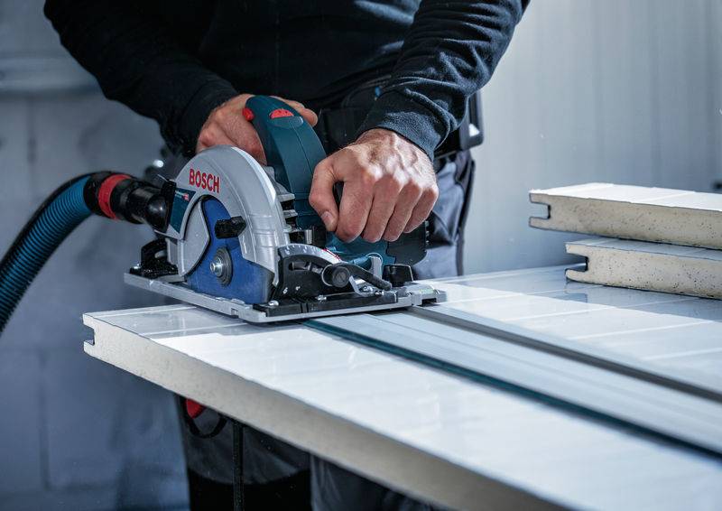 Eine Person benutzt eine Bosch-Elektrosäge, um ein großes Materialblatt auf einer Werkbank zu schneiden, was auf ein Bau- oder DIY-Projekt hindeutet.