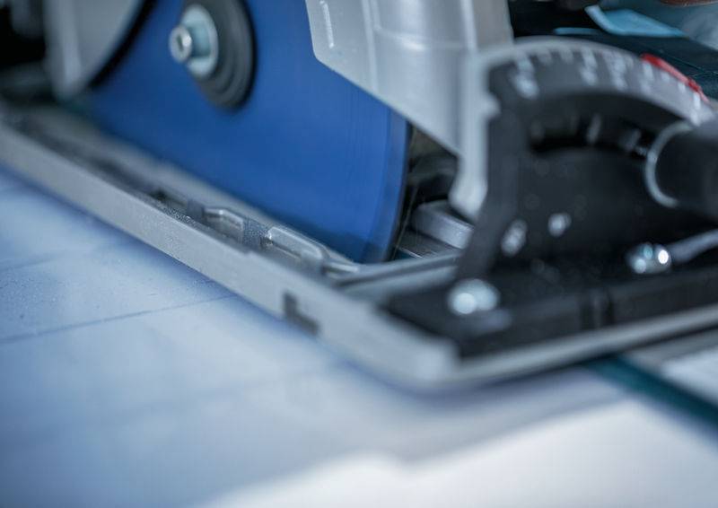 Ein Nahaufnahmebild einer sich bewegenden Kreissägeblatt, mit dem Fokus auf die Schneidkante und die Einstellungsskala, was auf Präzisionsarbeit hindeutet.