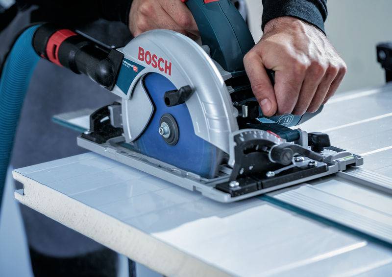 Eine Person nutzt eine Bosch-Kreissäge, um ein Stück Holz auf einer Metallführungsschiene zu schneiden und gewährleistet damit einen geraden und präzisen Schnitt.