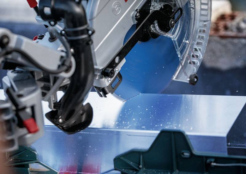 Eine Nahaufnahme einer Kreissäge, die durch ein Metallblech schneidet, mit deutlich sichtbaren blauen Funken. Der Fokus liegt auf der Wechselwirkung zwischen dem Sägeblatt und dem Metall.