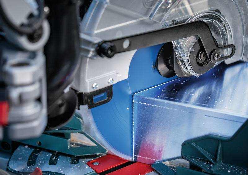 Eine Nahaufnahme einer Kreissäge, die durch ein Metallstück schneidet, mit umherfliegenden Funken und Schutzvorrichtungen an Ort und Stelle für Sicherheit.