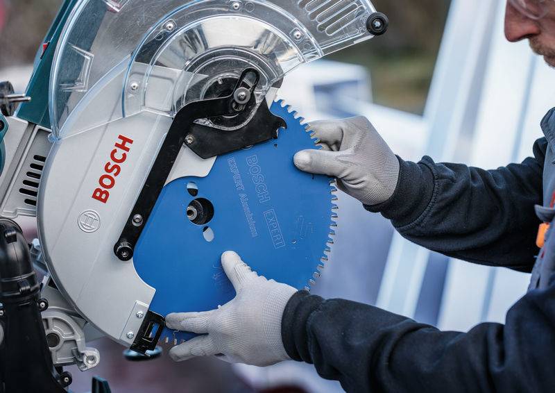 Eine Person mit Handschuhen installiert ein blaues Sägeblatt in ein Bosch-Elektrowerkzeug, was auf eine Einrichtungs- oder Wartungsaktivität mit dem Gerät hindeutet.