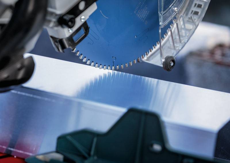 Eine Nahaufnahme eines Kreissägeblatts, das durch einen Metallblock schneidet, wobei die scharfen Zähne und der präzise Schnitt hervorgehoben werden.