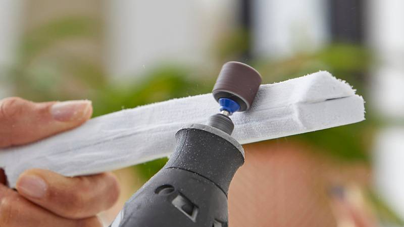 Eine Person benutzt ein Elektroschleifergerät mit einem Schleifaufsatz, um die Kanten eines weißen Schaumstofffings zu glätten.