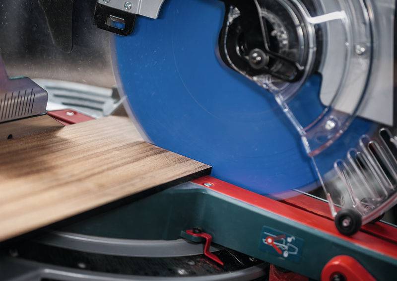 Eine Kreissäge schneidet ein Holzbrett mit Präzision auf einer Werkbank ab, wobei das rotierende blaue Sägeblatt und die Schutzvorrichtungen sichtbar sind.