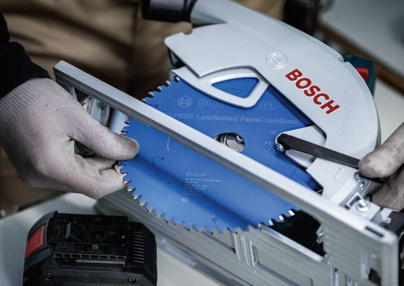 Person mit Handschuhen stellt ein Kreissägeblatt an einer Bosch-Säge ein, wobei ein Akku sichtbar ist, was die Sicherheit und Präzision des Werkzeugs unterstreicht.
