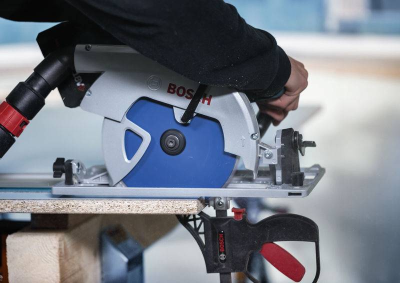 Eine Person benutzt eine Bosch-Kreissäge, um ein Stück Holz zu schneiden, wobei sie Präzision und Konzentration zeigt, während die rote Klammer das Holz an Ort und Stelle sichert.