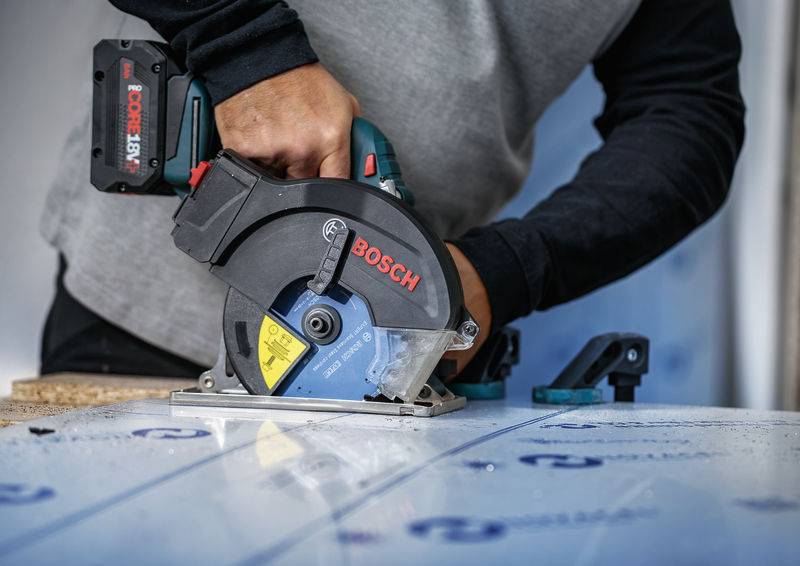 Eine Person, die eine Bosch-Elektrosäge verwendet, um durch ein Materialblatt zu schneiden, wobei der Fokus auf Präzision und Kontrolle in einer Baustelle liegt.