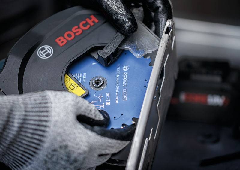 Eine Person, die Handschuhe trägt, wechselt ein Bosch-Sägeblatt an einer Kreissäge. Der Fokus liegt auf den Händen und der Säge und verdeutlicht sicheren Umgang mit Werkzeugen.