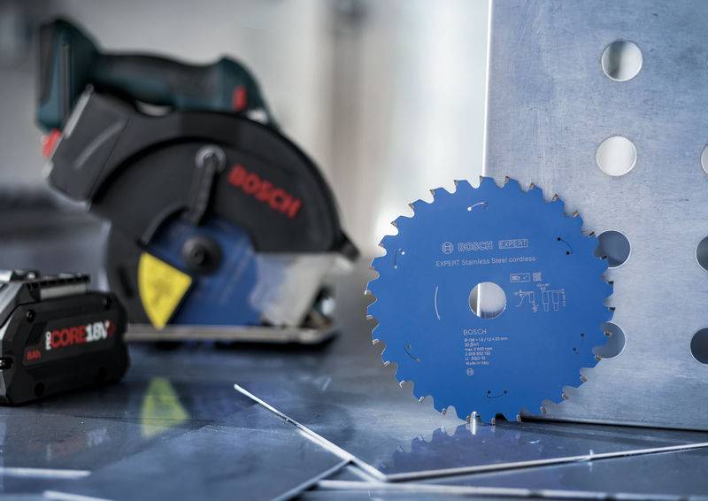 Eine Kreissägeblatt und Elektrowerkzeug auf einer metallischen Oberfläche. Das blaue Blatt ist mit Spezifikationen gekennzeichnet. Der Hintergrund zeigt Metallbleche mit Löchern.
