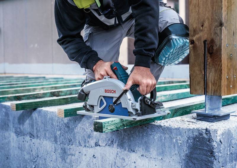 Person nutzt eine Kreissäge, um grüne Holzbalken auf einer Betonplatte zu schneiden. Der Fokus liegt auf der Präzision des Werkzeugs beim Schneiden.