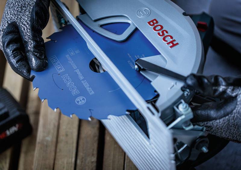 Eine Person mit Handschuhen baut ein Bosch-Kreissägeblatt in ein Elektrowerkzeug ein. Das Werkzeug ist silberfarben und trägt den Markennamen gut sichtbar.