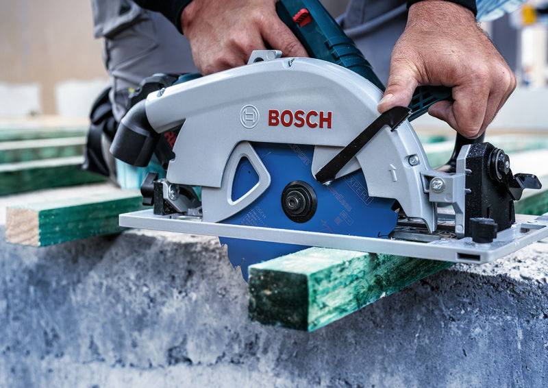 Bosch-Kreissäge, die ein Holzbrett durchschneidet, das von einem Arbeiter gehalten wird, auf einer Baustelle.