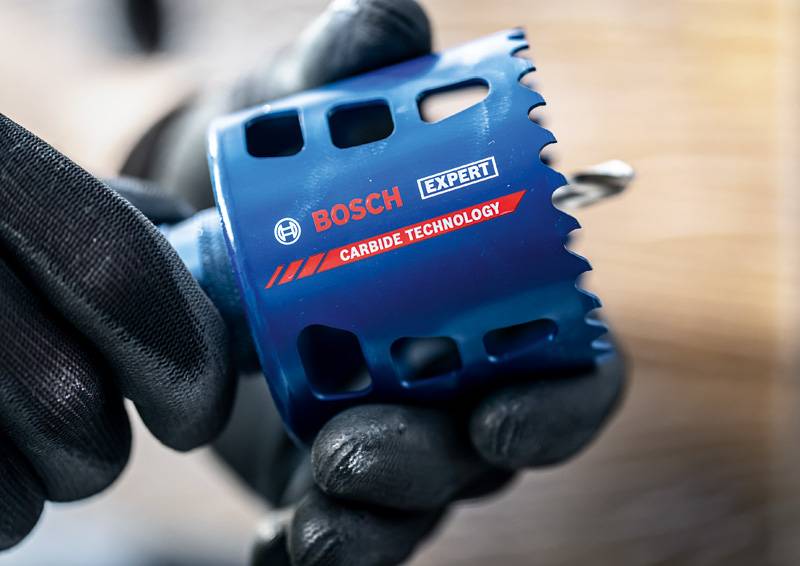 Eine Nahaufnahme einer behandschuhten Hand, die eine blaue Bosch Expert-Lochsäge mit der Aufschrift „Carbide Technology