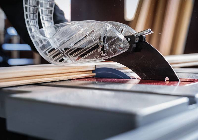 Eine Tischkreissäge mit einer durchsichtigen Schutzvorrichtung schneidet durch Holzbretter und hebt dabei Holzbearbeitung und Sicherheitsausrüstung hervor.
