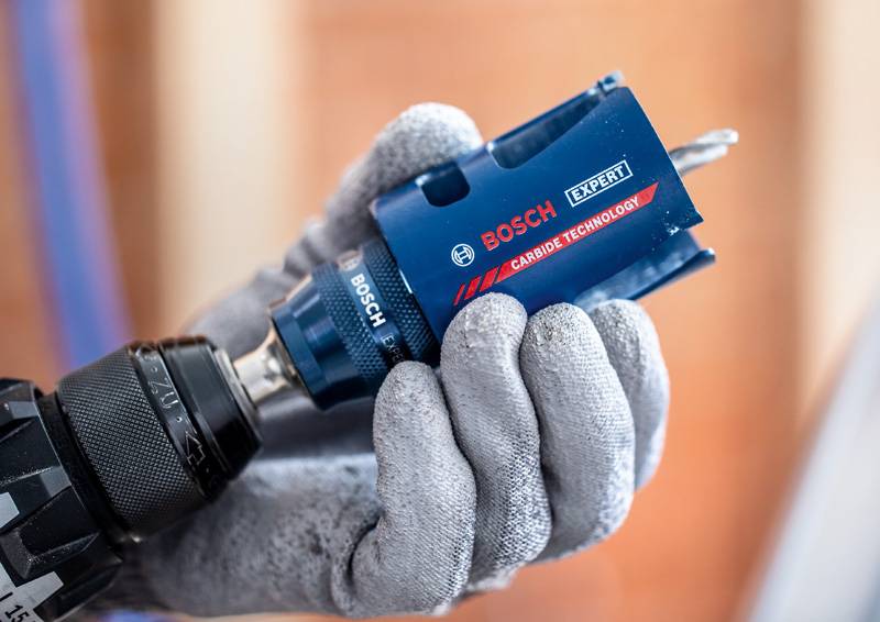 Eine behandschuhte Hand hält einen Bosch Expert Hartmetall-Bohrer, der an einem Bohrgerät befestigt ist, und hebt dessen Design und Branding hervor.