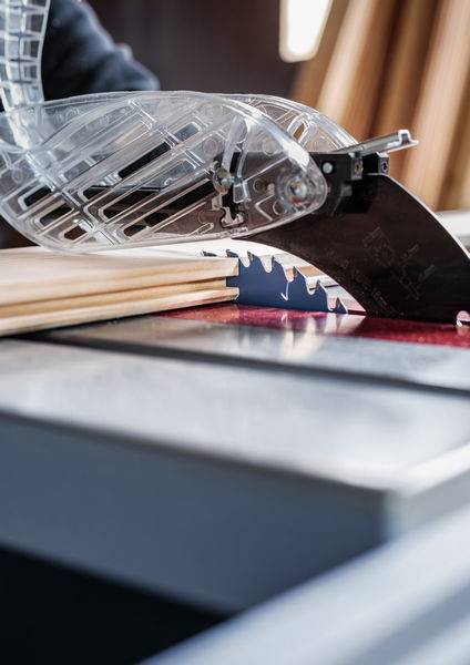 Eine Nahaufnahme einer Tischkreissäge, die durch Holzbretter schneidet, mit einer transparenten Schutzvorrichtung über dem Sägeblatt, die sichere Holzbearbeitungspraktiken hervorhebt.