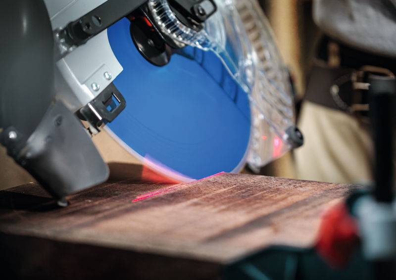 Eine Kreissäge mit einem blauen Blatt schneidet in ein Stück Holz ein, geführt von einer roten Laserlinie, die die Präzision der Holzbearbeitung demonstriert.