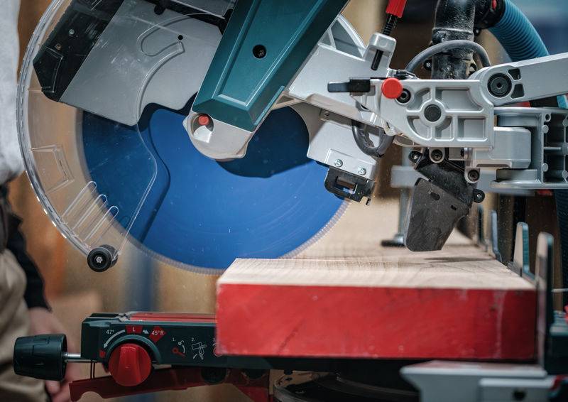 Ein kreissägeblatt schneidet ein holzbrett in einer werkstatt. Das blaue kreisförmige blatt ist in bewegung, mit sicherheitsvorkehrungen an ort und stelle.