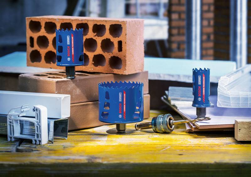 Assortierte Bosch-Lochsägen auf einem Holztisch ausgestellt, mit Ziegeln und Baumaterialien im Hintergrund, die ihre Verwendung in der Maurerarbeit zeigen.