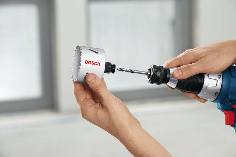 „Zwei Hände befestigen eine Bosch-Lochsäge an einer Elektrobohrmaschine in Innenräumen, möglicherweise zur Vorbereitung von Bohrarbeiten.