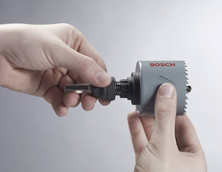 Hände, die ein Bosch-Lochsäge-Set und Bohraufsatz zusammenbauen, wobei der Werkzeugaufbauprozess demonstriert wird.