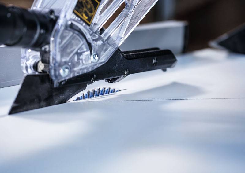 Eine Nahaufnahme einer Tischkreissäge, die durch weißes Material schneidet, mit teilweise sichtbaren blauen Zähnen, was auf den Betrieb einer Präzisionsmaschine hindeutet.