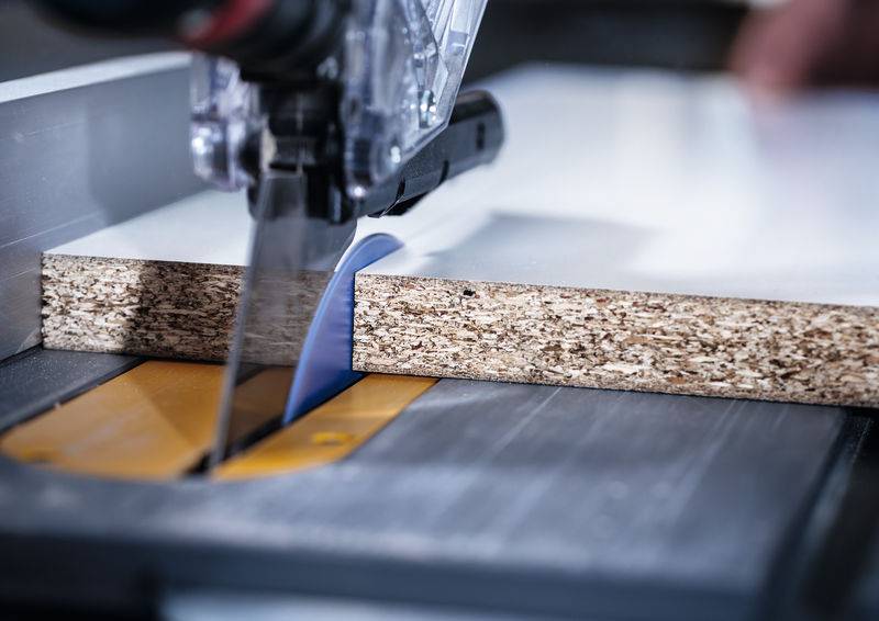 Eine Elektrosäge schneidet durch ein Stück Spanplatte, wobei das Blatt auf einer Tischkreissäge durch das Holz fährt.