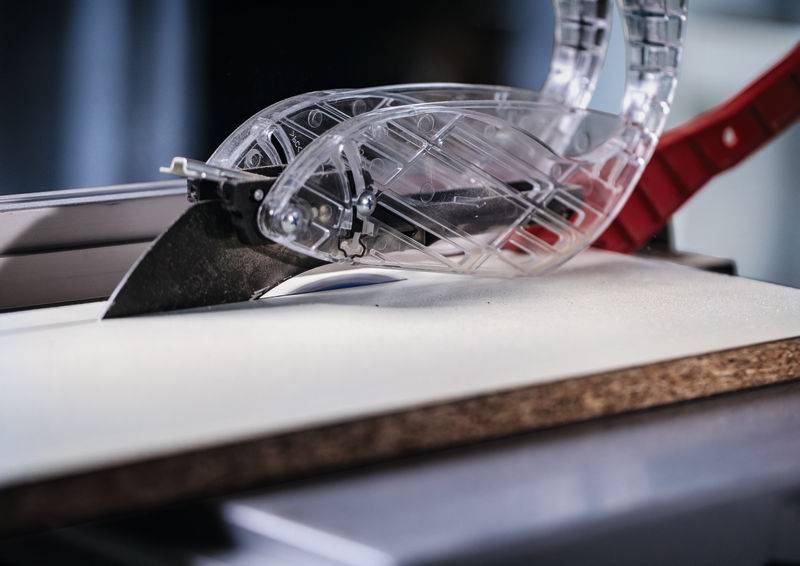 Eine Kreissäge mit durchsichtigem Schutzschild schneidet durch ein Holzbrett.