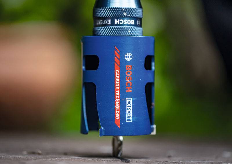 Ein blau beschichtetes Bosch-Hartmetall-Technologie-Werkzeug mit einem Bohrer, platziert auf einer Holzoberfläche, verwendet für präzise Bohraufgaben.