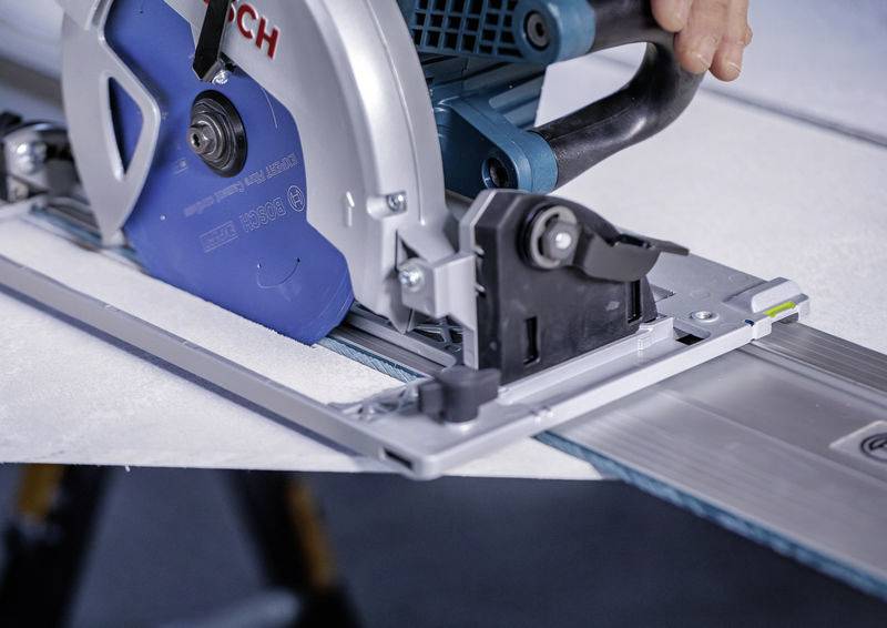 Eine Kreissäge, die durch ein Materialblatt auf einer Metallschiene schneidet und präzise und gerade Schnitte anzeigt. Eine Hand einer Person führt die Säge.