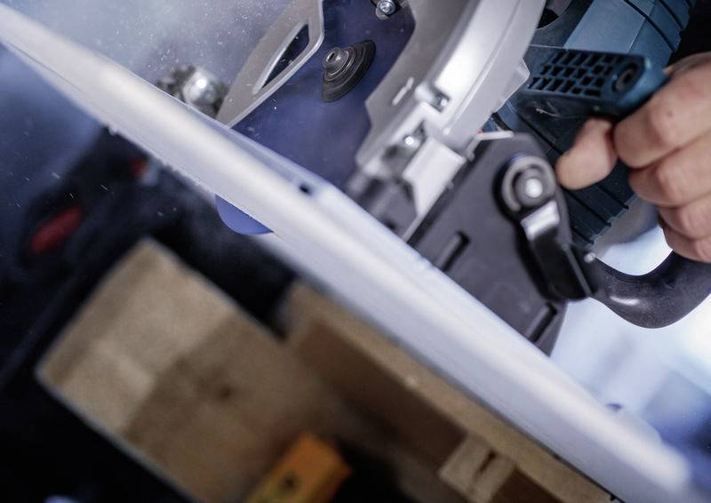 Eine Person, die eine Kreissäge zum Schneiden eines Holzstücks benutzt, mit Fokus auf das Sägeblatt und die Handpositionierung für präzises Schneiden.