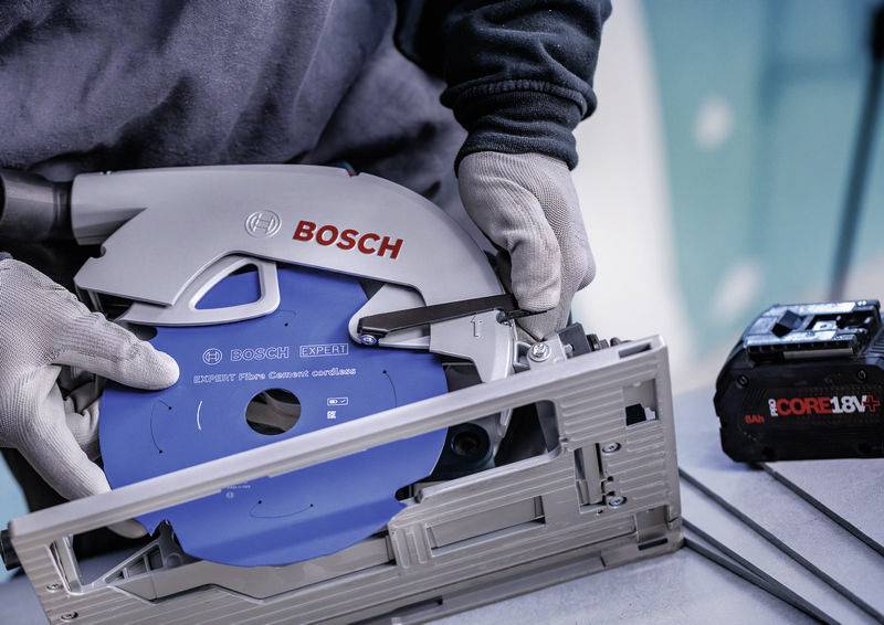 Eine Person mit Handschuhen stellt eine Bosch-Säge mit blauem Blatt auf einer Werkbank ein und bereitet sie zur Verwendung vor, was auf einen Fokus auf Sicherheit und Präzision hindeutet.