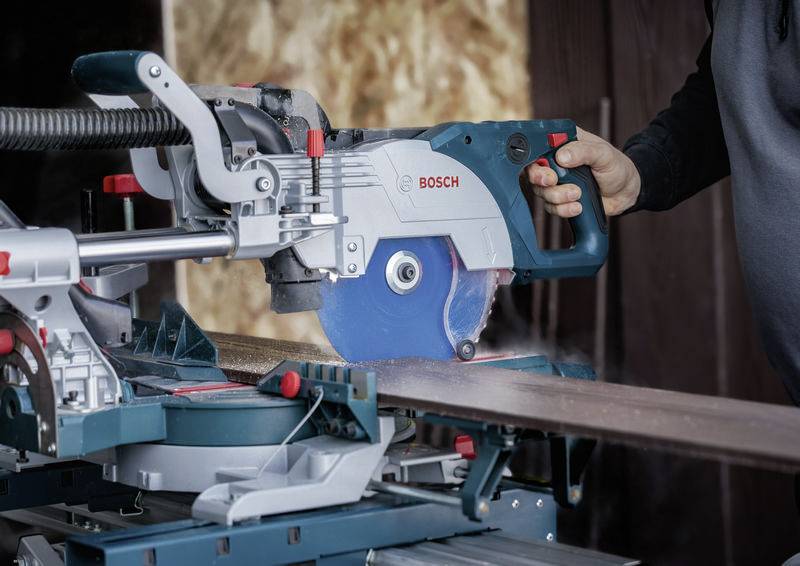 Eine Person nutzt eine Bosch-Gehrungssäge, um ein Holzbrett zu schneiden, und demonstriert dabei eine Schreinerei-Aufgabe in einer Werkstatt-Umgebung.