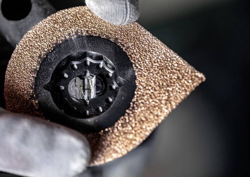 Eine behandschuhte Hand hält ein Mehrzweck-Oszillationsblatt mit einer strukturierten Kupferoberfläche, das sich zum Schleifen oder Mahlen von Materialien eignet.