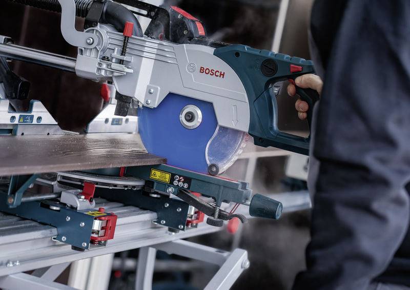 Eine Person, die eine Bosch-Elektrosäge bedient, um ein Holzbrett auf einem Gehrungssägeständer zu schneiden, mit Fokus auf Präzision und Sicherheit.