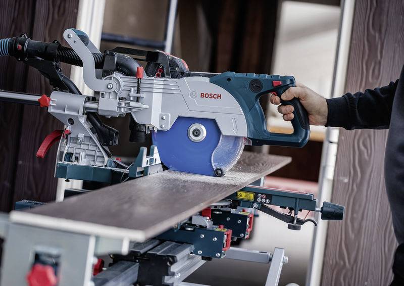 Eine Person bedient eine Bosch-Kreissäge und schneidet ein auf einer Werkbank gehaltenes Holzbrett. Die Einstellung deutet auf eine Zimmer- oder Bauaufgabe hin.