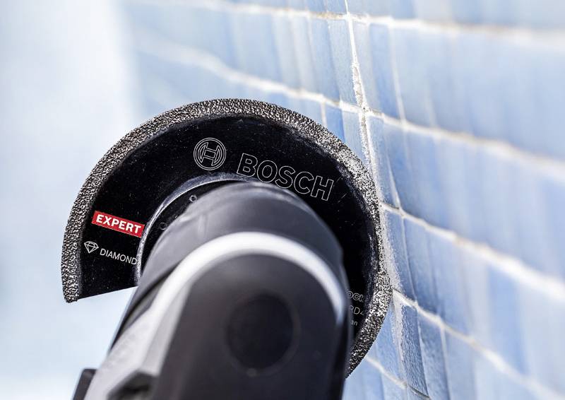 Ein Bosch-Diamanttrennscheiben-Fliesenschneider wird beim Durchschneiden einer hellblauen Fliesenoberfläche gezeigt und demonstriert seine Präzision bei Konstruktionsaufgaben.