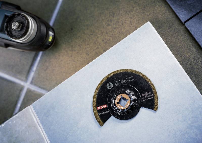 Ein Elektrowerkzeug ist in der Nähe einer Kreissägeblatt auf einer Kachelfläche positioniert, was auf einen Arbeitsbereich für Schneid- oder Konstruktionsaufgaben hindeutet.