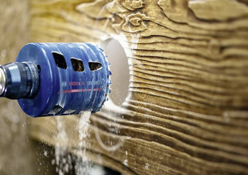 Ein blauer Lochsäge-Bohrer erzeugt ein kreisförmiges Loch im Holz und verteilt Holzspäne.