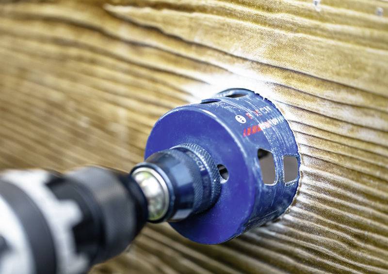 Ein Bohrer mit einem Lochsägeblatt schneidet durch eine Holzoberfläche und erzeugt dabei ein kreisrundes Loch.