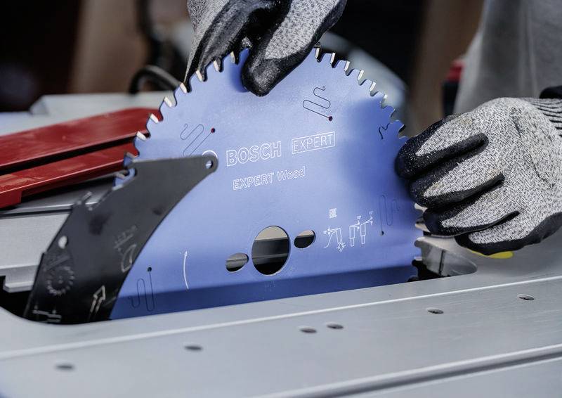 Eine Person mit Handschuhen montiert ein Bosch-Expert-Sägeblatt auf einer Tischkreissäge und konzentriert sich dabei auf präzise Ausrichtung und Sicherheit.