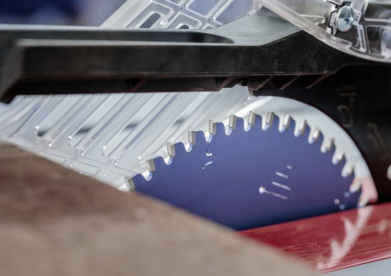 „Eine Nahaufnahme eines Kreissägeblatts, das teilweise von einer transparenten Schutzvorrichtung bedeckt ist und scharfe Zähne sowie eine rote Basis zum Holzschneiden zeigt.