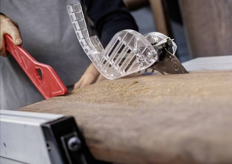 Eine Person benutzt eine Tischkreissäge mit einem roten Schiebestab, um ein Holzbrett sicher durch das Sägeblatt zu führen und dabei Präzision und Sicherheit zu gewährleisten.