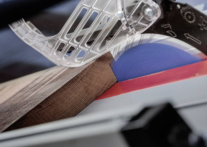 Eine Kreissägeblatt schneidet durch ein Stück Holz, mit einer Schutzvorrichtung an Ort und Stelle. Das Holz hat eine dunkle Oberfläche und abgeschrägte Kanten.