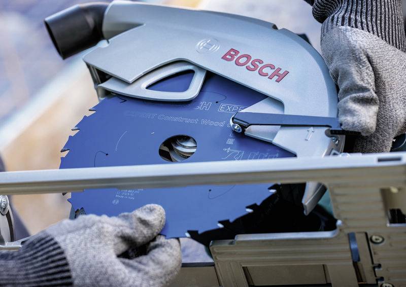 Eine Person, die Handschuhe trägt, baut ein blaues rundes Sägeblatt in ein Bosch-Elektrowerkzeug ein, im Freien.