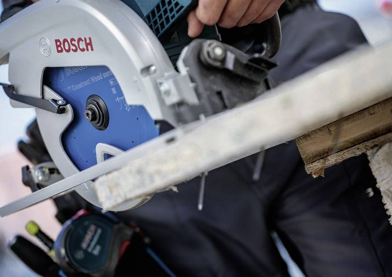 Ein Bauarbeiter nutzt eine Bosch-Kreissäge, um ein Holzbrett zu schneiden, wobei er Konzentration und Präzision in der Zimmermannsarbeit demonstriert.